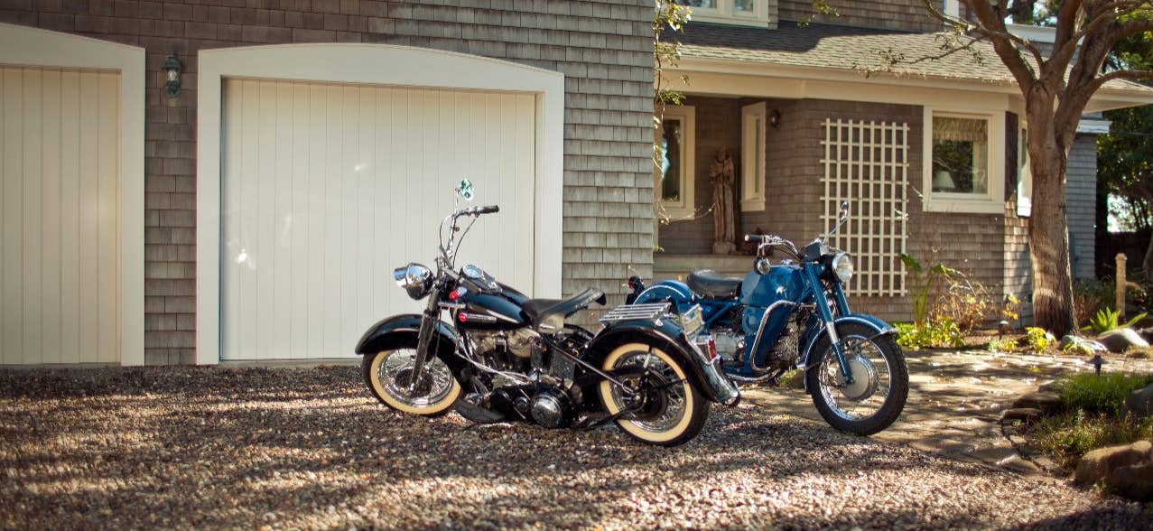 Two motorcycles park outside a house garage