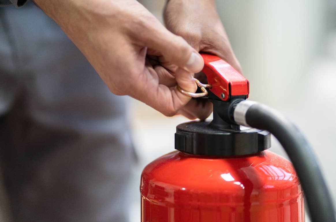 Hands pulling pin out from fire extinguisher
