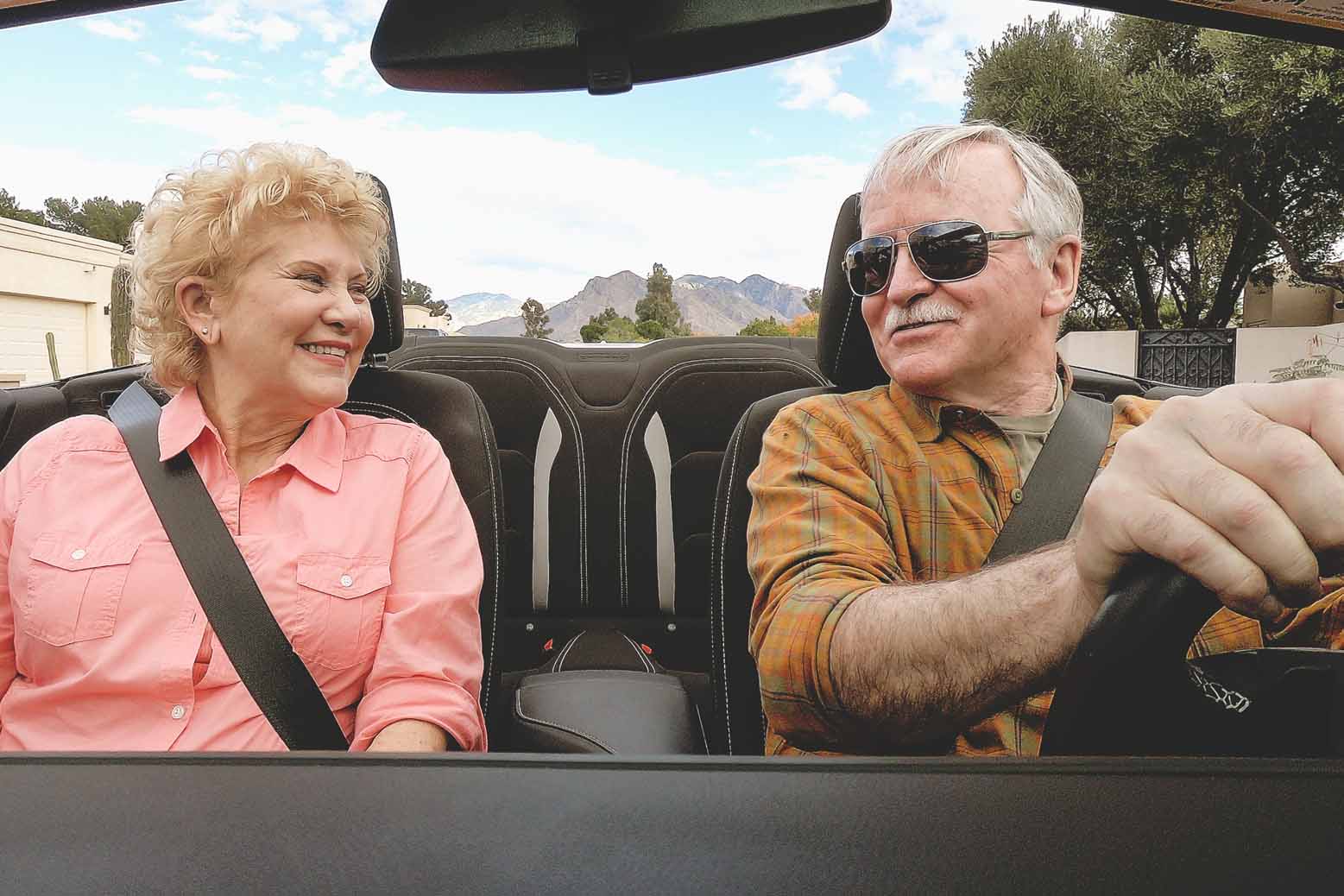 Older man and woman happily driving their convertible on a sunny day.